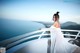 A woman in a white dress standing on a balcony overlooking the ocean.