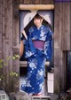 A woman in a blue and white kimono standing in front of a wooden door.