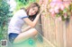 A woman sitting on the ground next to a wooden fence.