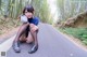 A young woman sitting on the side of a road in the woods.