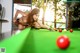 A naked woman is playing pool on a green table.