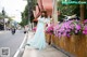 A woman in a long blue dress walking down the street.